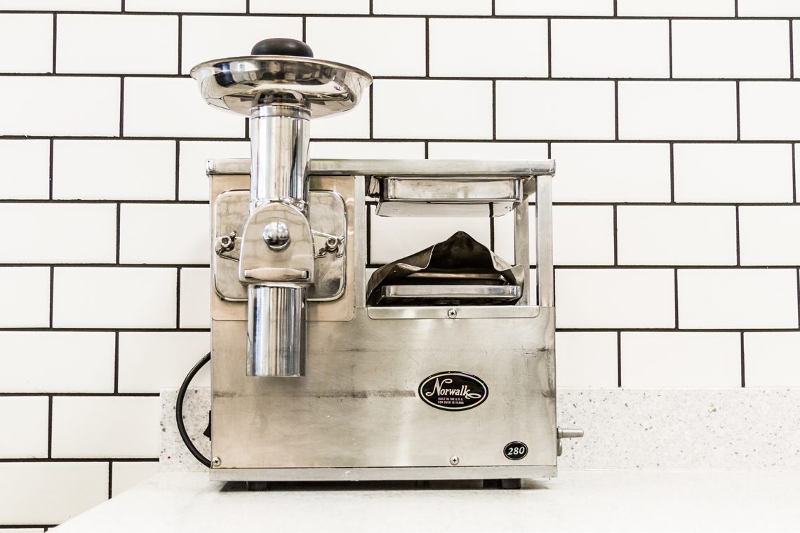 The hydraulic juice press at The Juice Bar against white subway tile